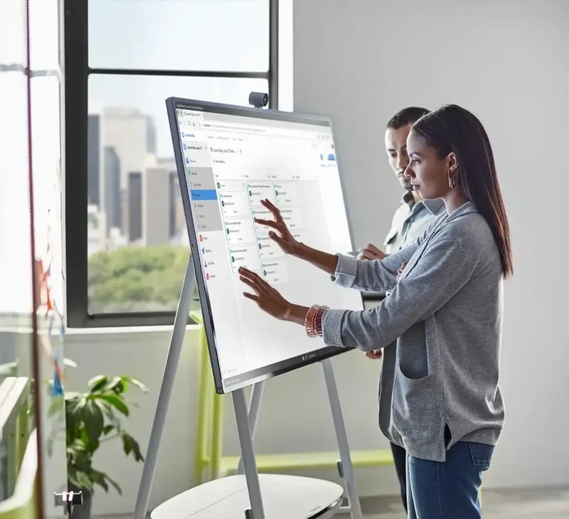 Dos colaboradores de trabajo haciendo uso de una herramienta de Surface Hub 2S en una oficina "Modernworkplace"